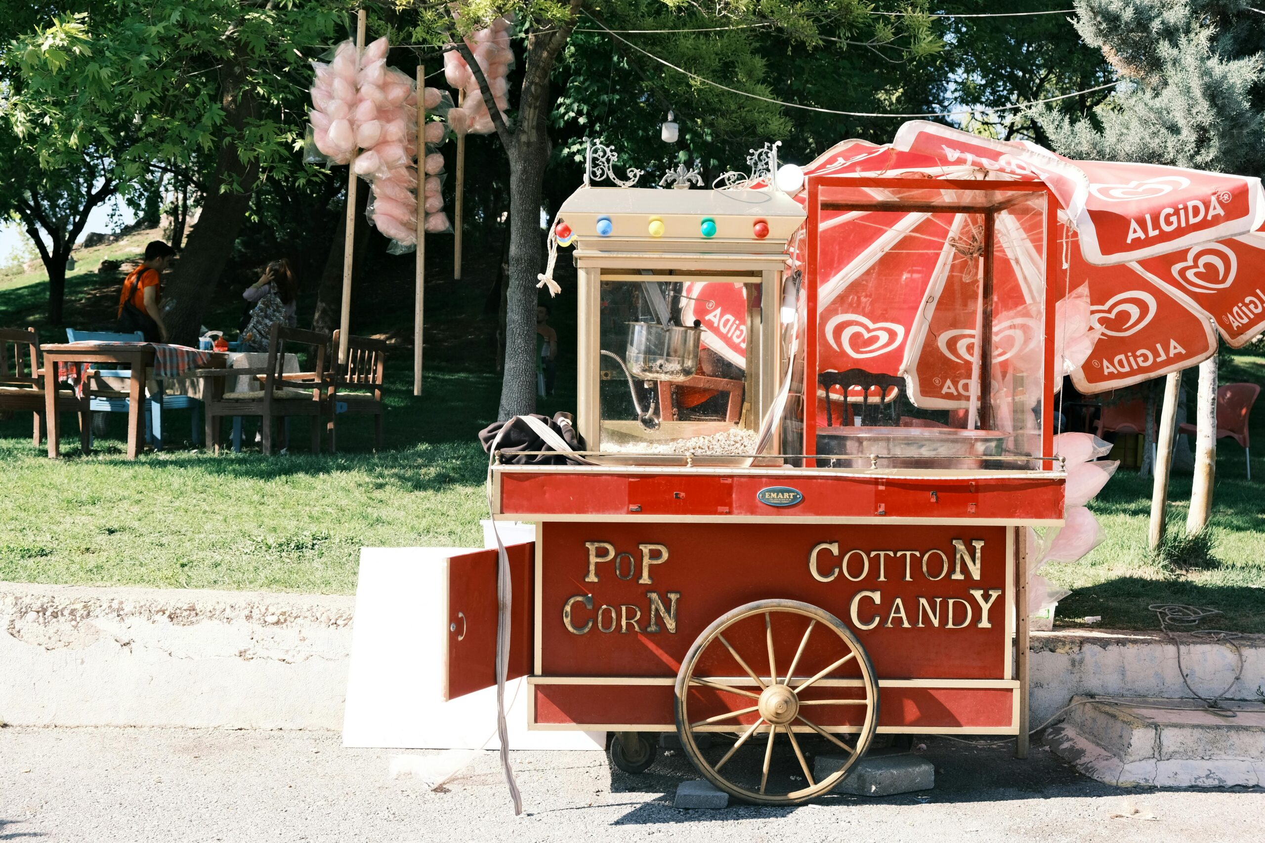 A charming vintage cotton candy and popcorn cart outdoors in a park setting offering nostalgic street food.